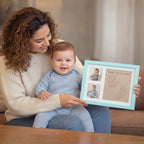 Woman holding a baby and a framed keepsake with handprints and a photo of the baby.