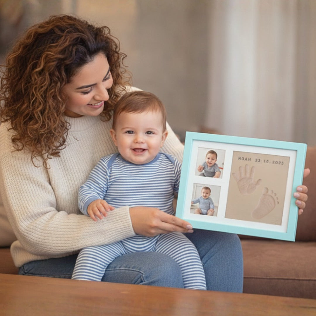 Woman holding a baby and a framed keepsake with handprints and a photo of the baby.